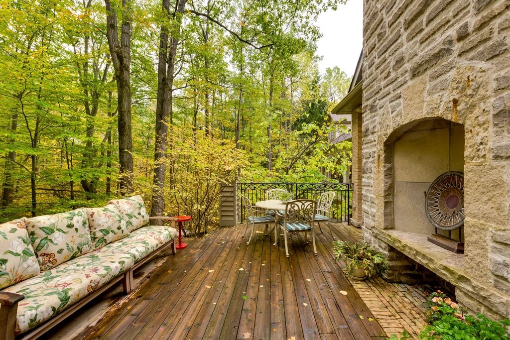 Stained wood deck beside a stone house, surrounded by hardwood trees