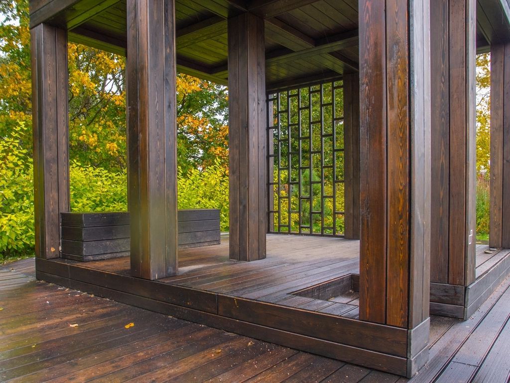 Stained wood posts and floor of an open pavilion beside trees